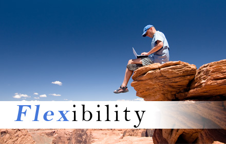 Image of a man in cap and shorts sitting on the edge of a rock face in a remote location and working on a laptop, and with the word "flexibility" over the image