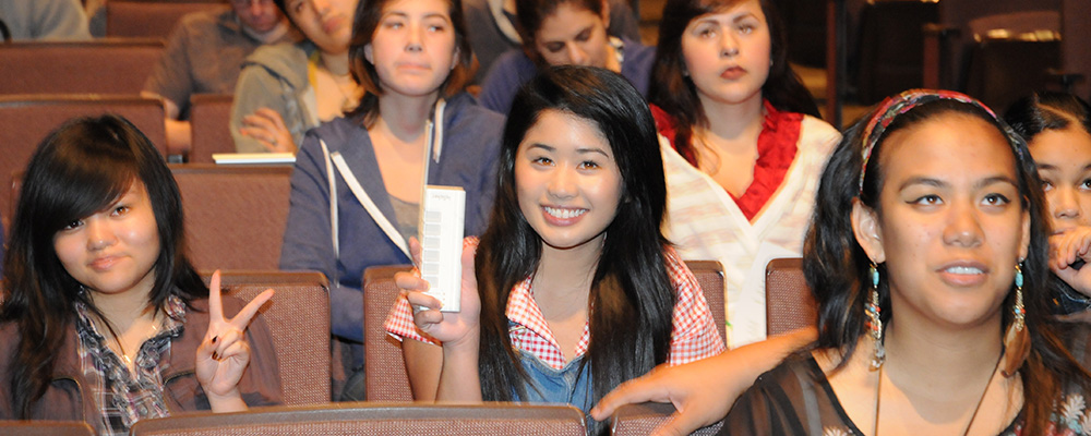 Group of students in the CSULB University Theater (UT-108) with the one in the center holding up an iClicker and smiling.