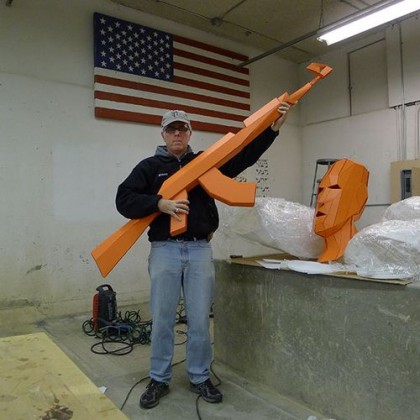 Joseph DeLappe holding an oversized rifle made out of cardboard polygons from the game America's Army