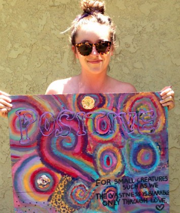 a woman holding and standing behind a painting of Kandinsky-esque circles with an inspirational quotation painted over