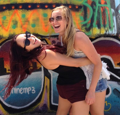 Two women in front of the Venice Beach Art Walls. One hugs the other and hoists her into the air.