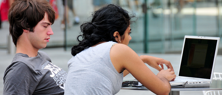 a college age man and woman work at a laptop in an open air environment