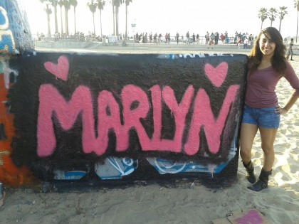 Photo of Marlyn Castillo standing next to her name "Marlyn" painted on a wall at the Venice Beach Legal Art Walls in Venice Beach, CA