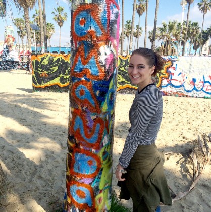 Photo of Amanda Bjornstad at Venice Beach, California, at the Venice Art Walls standing next to a palm tree that has her name written vertically in blue and red letters