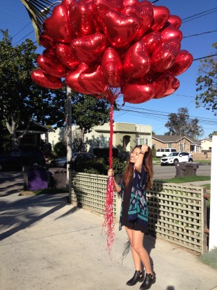 Mary Quach stands on the sidewalk with dozens of giant red mylar heart balloons that she will give to friends and strangers