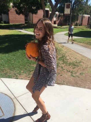 Sierra Putman on the sidewalk and holding a pumpkin and laughing.