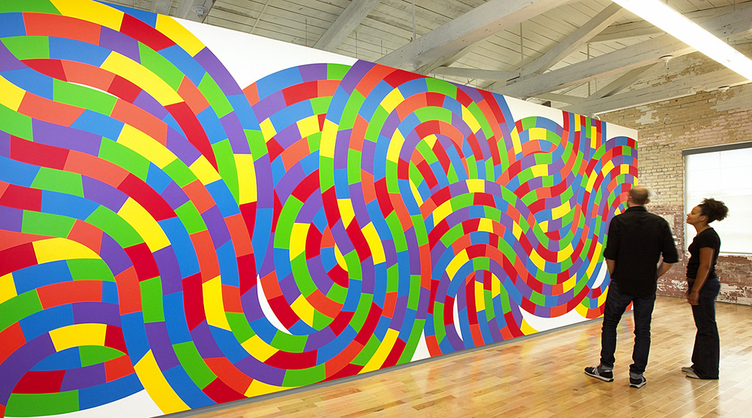 photo of 2 people standing before a large, curving, Sol LeWitt wall drawing